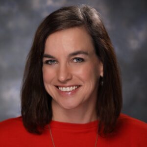 Smiling woman with brown hair in a red shirt against a neutral backdrop.
